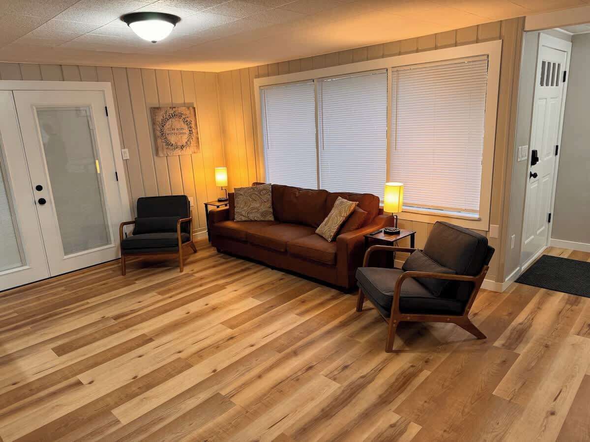 A room with a wooden floor, a brown sofa, two armchairs, and a small table.