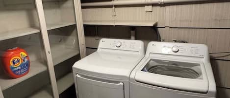 A laundry room with a washing machine and dryer, a shelf with a Tide detergent bottle, and a white cabinet.