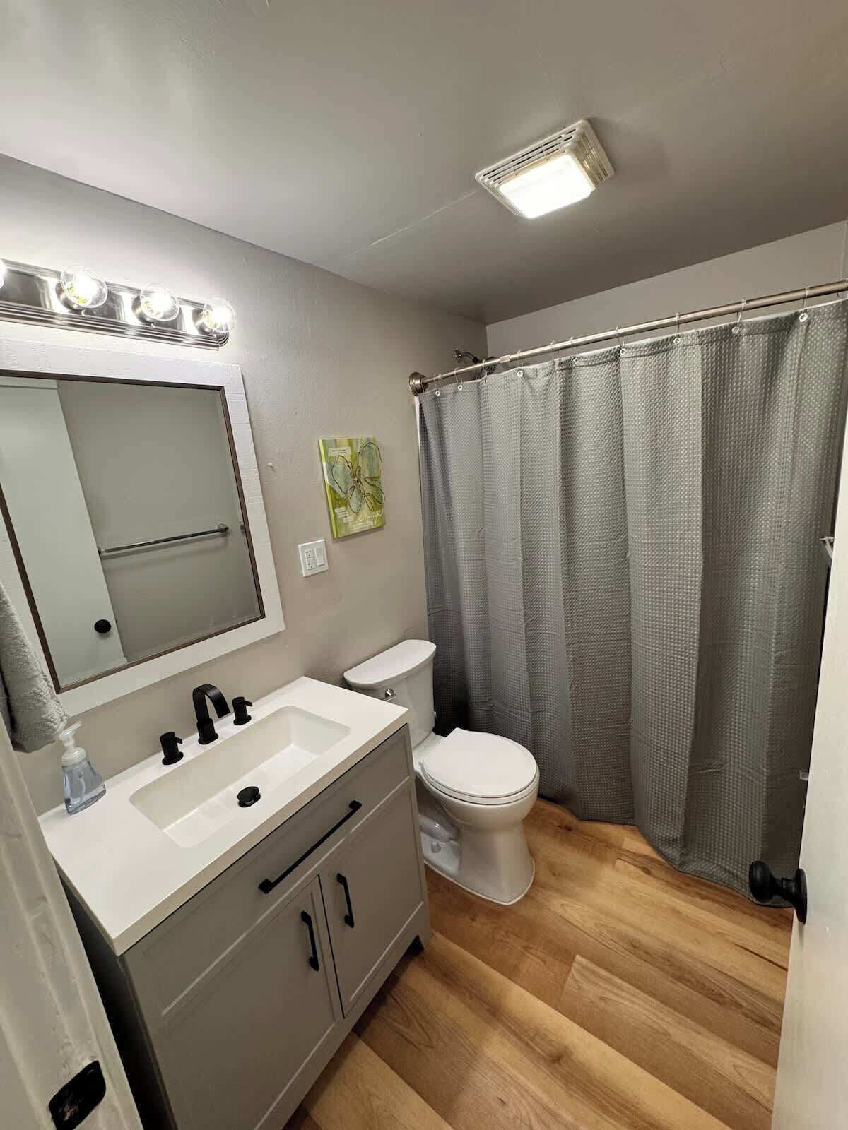 Baño con lavamanos blanco, espejo, inodoro, cortina de ducha y lámpara en el techo.