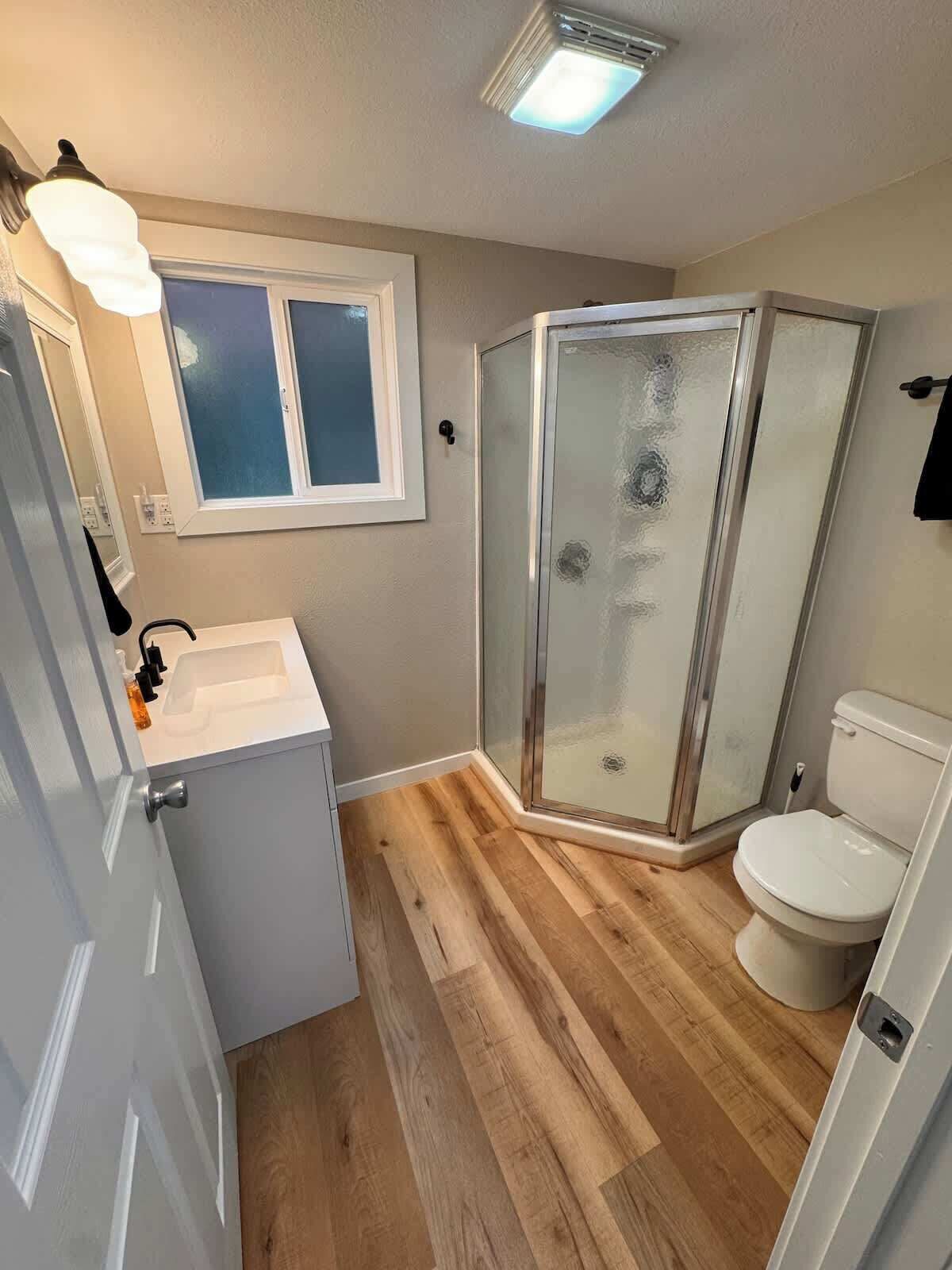 A bathroom with a shower, toilet, sink, and mirror.