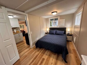 Un dormitorio con cama, mesitas de noche, una ventana y una puerta que da a un baño.