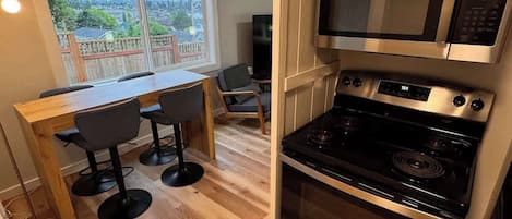 Une cuisine compacte donnant sur l’extérieur, un coin repas avec une table et des chaises, ainsi qu’un four et un micro-ondes encastrés.