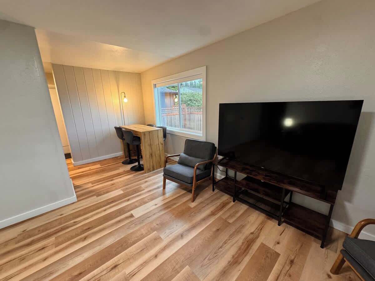 A living room with a flat-screen TV, a wooden dining table, and a chair.