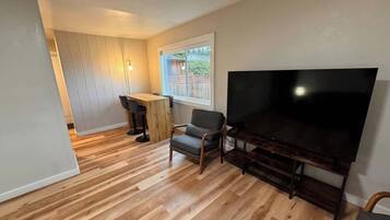 A living room with a flat-screen TV, a wooden dining table, and a chair.