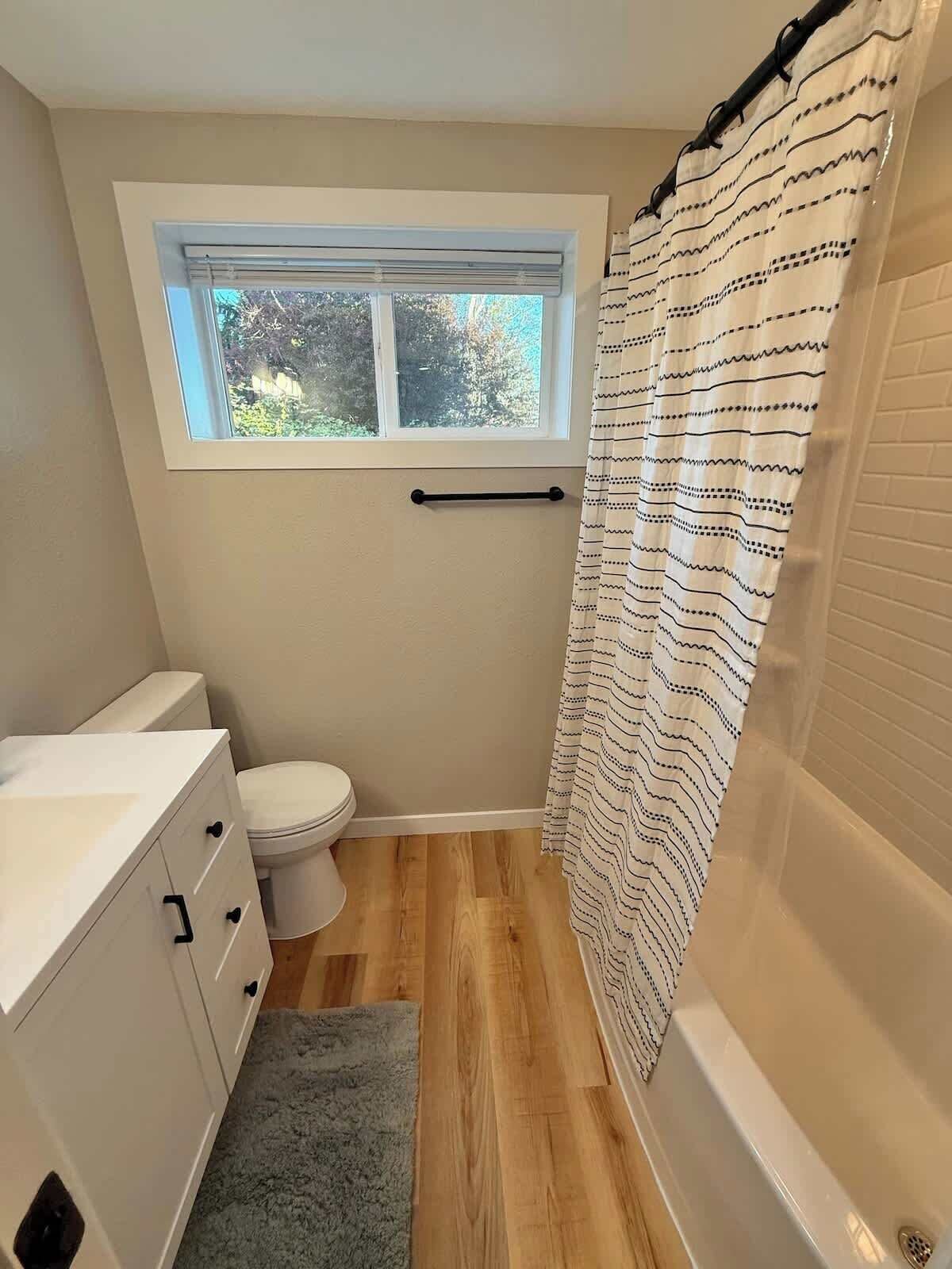 Une petite salle de bain avec une fenêtre, des toilettes, un lavabo et un rideau de douche.