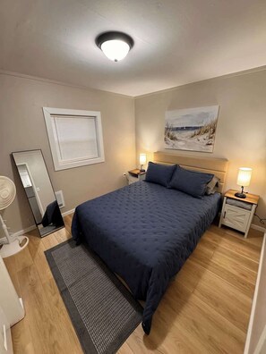Et soveværelse med seng, sengeborde, et spejl, et vindue med rullegardiner og en loftlampe.