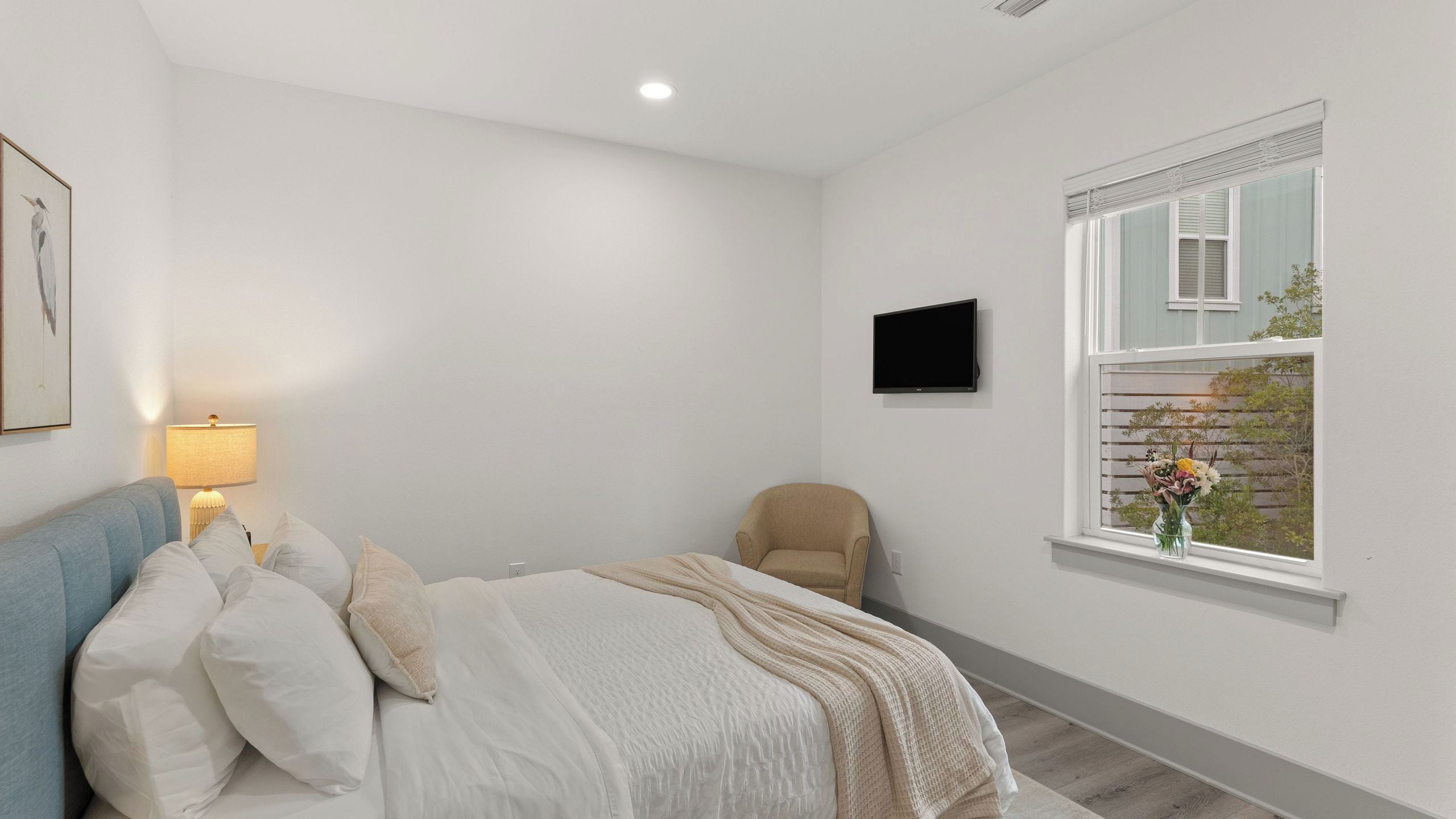 A bedroom with a bed, a chair, a TV, and a window with a view.