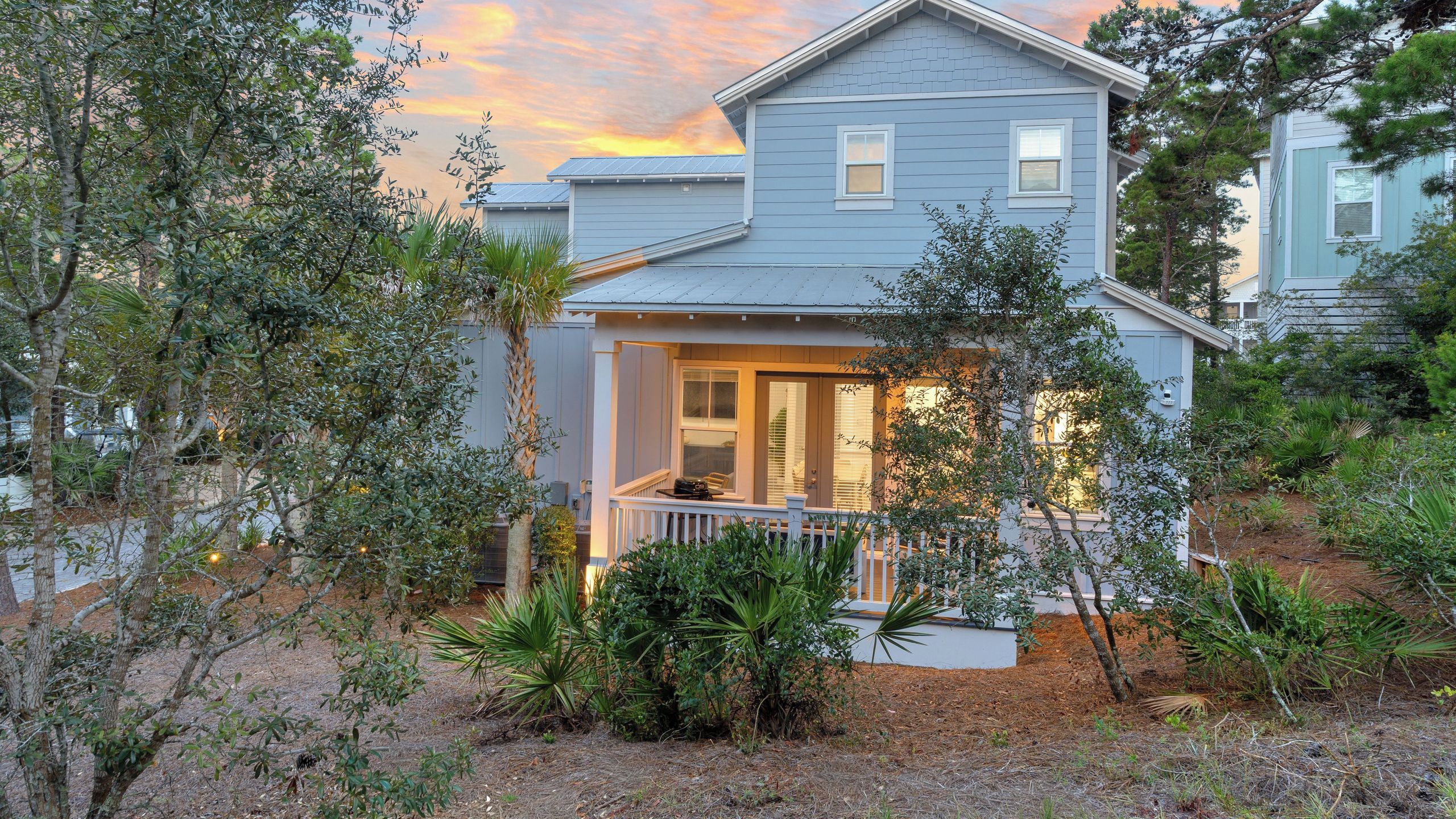 A two-story house with a porch and a small deck, surrounded by various trees and shrubs.
