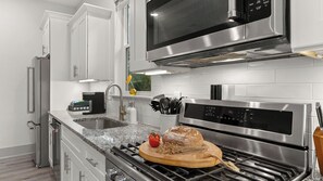Eine moderne Küche mit Edelstahlgeräten, einer Granitabdeckung und einem Holzschnittbrett mit Brot und einer Tomate.