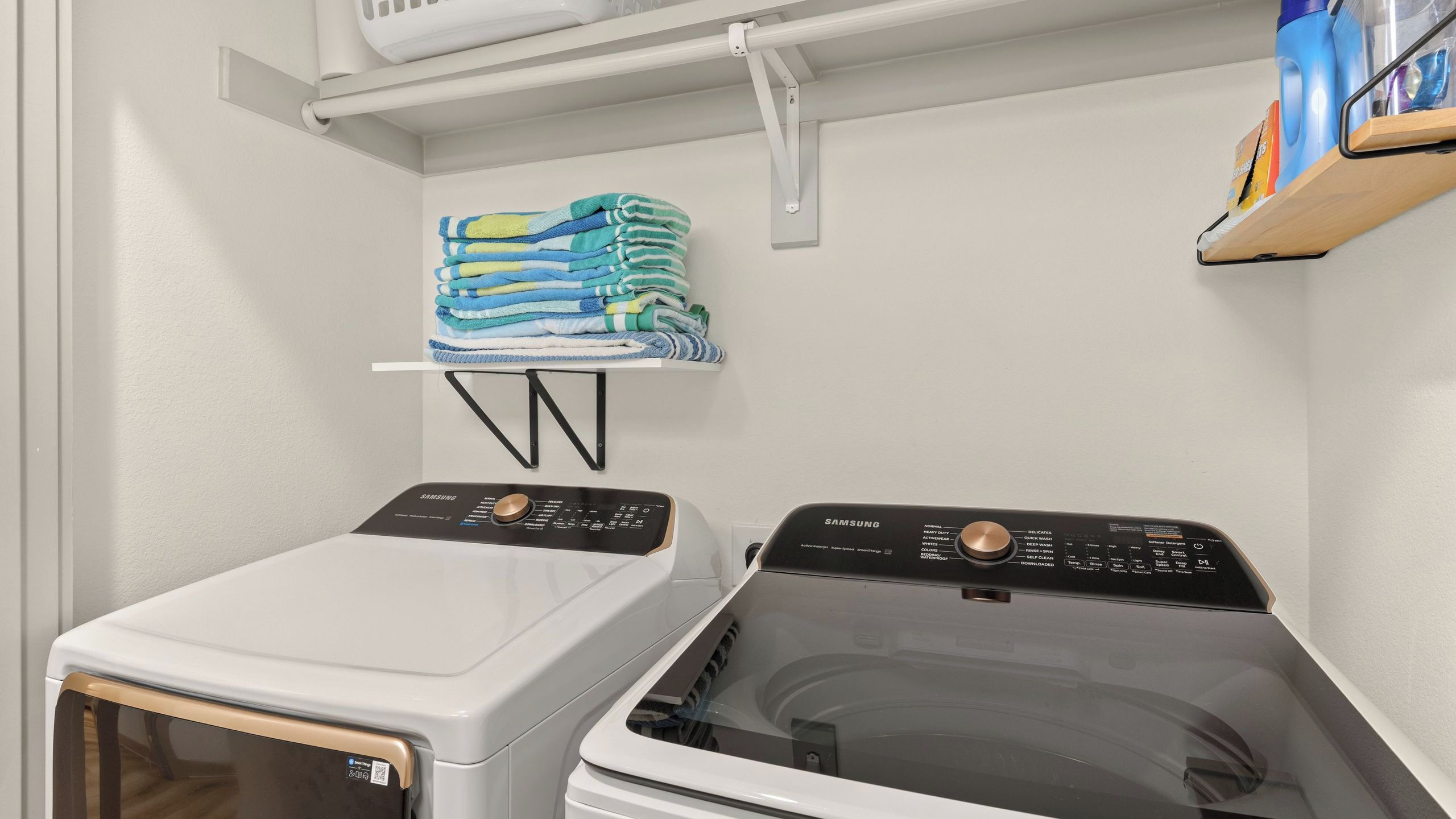 A laundry room with a front-loading washing machine and a stacked pile of folded towels on a small shelf.