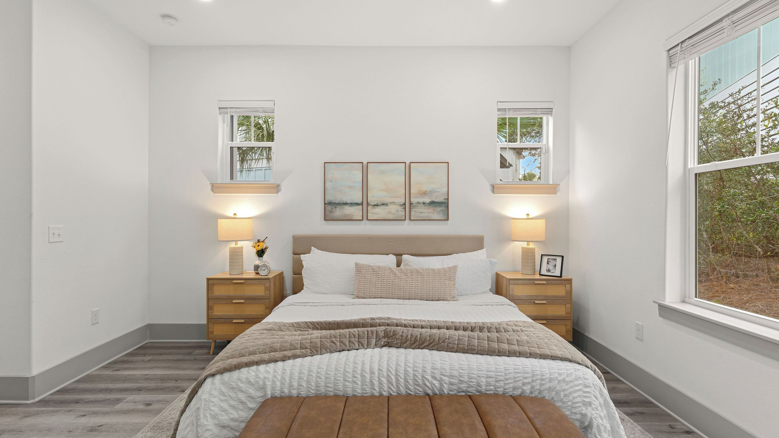 Un dormitorio con cama, mesitas de noche, lámparas y una obra de arte en la pared.