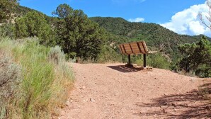 A dirt path leading to a wooden bench with a sign, surrounded by greenery and hills. - River View Ridge w/ Hot Tub/Dog Friendly (Glenwood Springs)