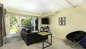 A room with a sliding glass door leading to a garden, a black sofa, a small table, a TV mounted on the wall, and a chair. - River View Ridge w/ Hot Tub/Dog Friendly (Glenwood Springs)