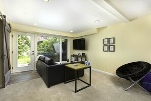 A room with a sliding glass door leading to a garden, a black sofa, a small table, a TV mounted on the wall, and a chair. - River View Ridge w/ Hot Tub/Dog Friendly (Glenwood Springs)