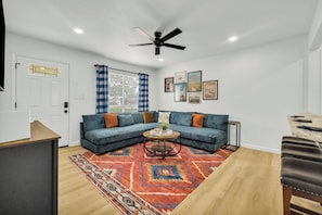 Una sala de estar con un sofá modular, una mesa de centro, un tapete estampado y un ventilador de techo.