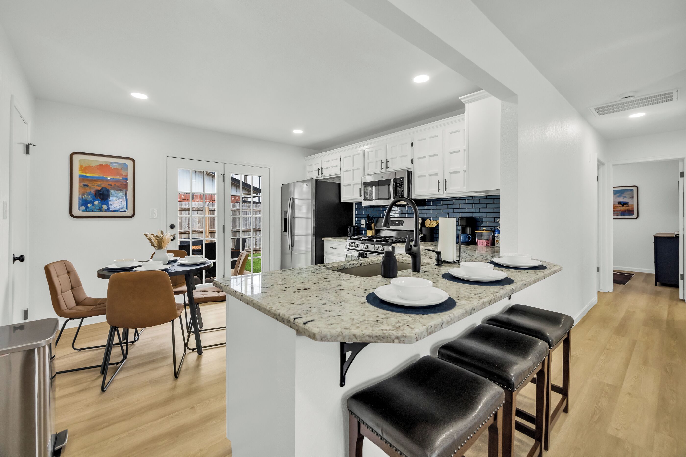 A modern kitchen with white cabinets, a central island with stools, and a dining area with a table and chairs.