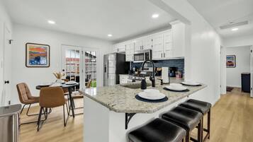 A modern kitchen with white cabinets, a central island with stools, and a dining area with a table and chairs.