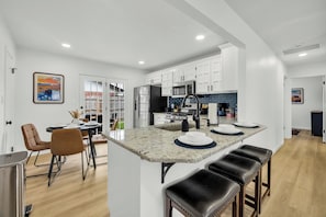 Una cocina moderna con armarios blancos, una isla central con taburetes y un comedor con mesa y sillas.