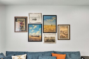 Un mur orné de six tableaux encadrés, un canapé bleu avec des coussins et un mur blanc.