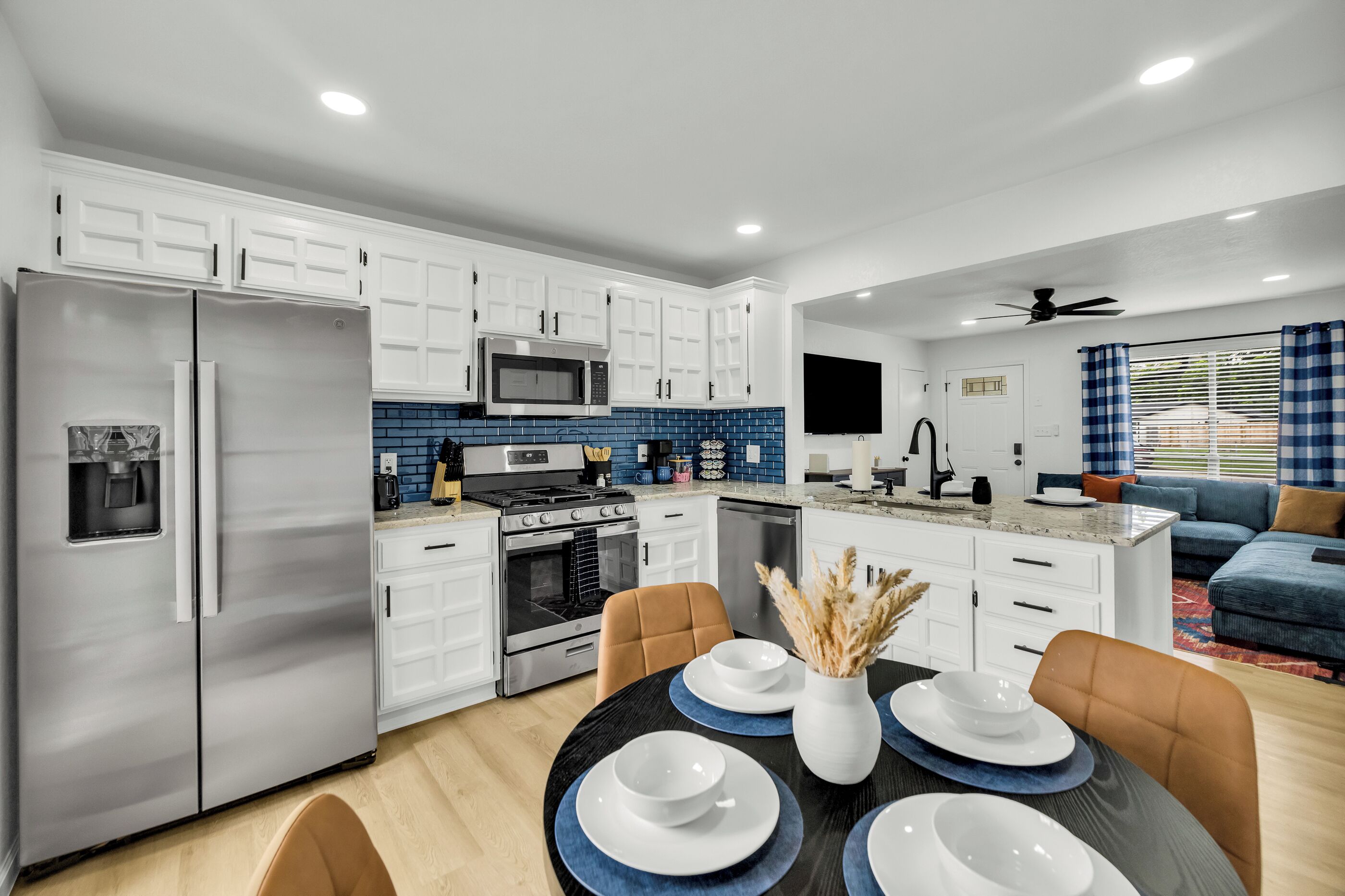 A modern kitchen with white cabinets, stainless steel appliances, and a blue tiled backsplash.