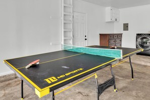 Une table de ping-pong portant la marque « MD SPORTS », une porte blanche avec une échelle, et un lave-linge en arrière-plan.