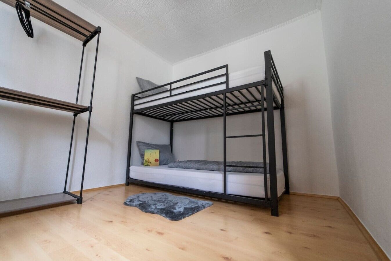 Una cama litera en una habitación con suelo de madera y paredes blancas.