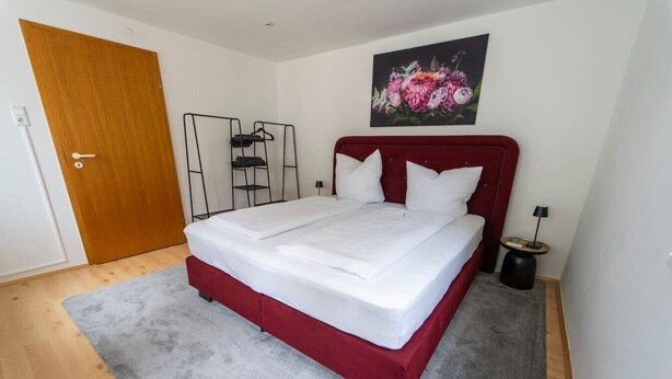 A neatly made bed with white linens in a room with a wooden floor and a grey carpet. - "Ferro" – historical and modern, with a balcony (Günzburg)