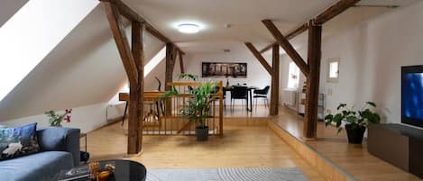 A spacious loft with exposed wooden beams, a dining area, and a seating area with a coffee table.