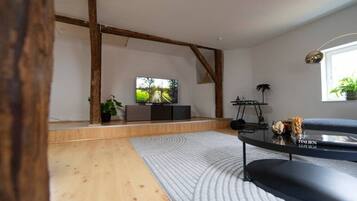 Ein modernes Wohnzimmer mit Flachbildfernseher, Holzbalken, einer Couch und einem Couchtisch.