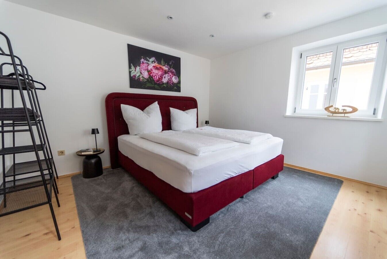 A bedroom with a bed, a ladder, a nightstand, a lamp, a window, and a painting on the wall.