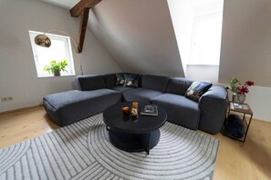 A modern living room with a sectional sofa, a round coffee table, a small side table with a vase, and a window with plants. - "Ferro" – historical and modern, with a balcony (Günzburg)