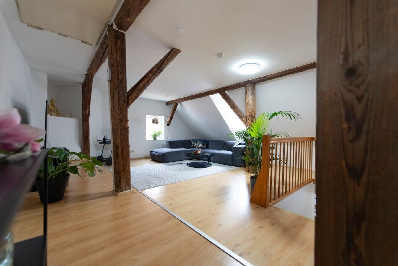 Ein Loft-Zimmer mit freiliegenden Holzbalken, einem dunkelgrauen Sofa, einem kleinen runden Tisch und einem Blumentopf.