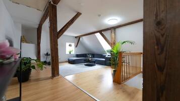 Ein Loft-Zimmer mit freiliegenden Holzbalken, einem dunkelgrauen Sofa, einem kleinen runden Tisch und einem Blumentopf.