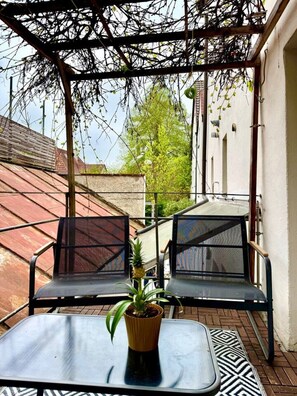 Un espacio al aire libre con dos sillas, una mesa, una planta en maceta y una estructura de pérgola.