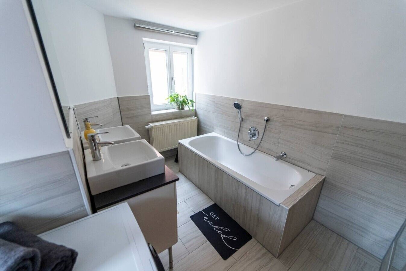 A modern bathroom with a bathtub, two sinks, and a window.