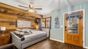 A bedroom with a bed, wooden wall paneling, a ceiling fan, a door with a window, and a wall-mounted light fixture. - Escape to your own private luxury estate in the heart of Sedona Wine Country. Designed for groups of up to 14 guests, The Reserve offers a rare combination of relaxation, connection, and adventure. Enjoy pickleball matches, evening hot tub gatherings (Cornville)