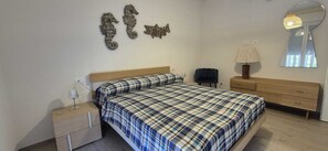 Ein Schlafzimmer mit Bett, Nachttischen, einer Lampe, einem Sessel, einer Kommode und Wanddekorationen.
