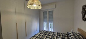 Et soveværelse med seng, garderobeskab, et vindue med persienner og en hængende lampe.