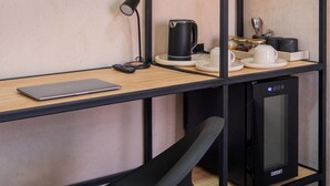 Un espacio de trabajo moderno con escritorio, una silla de oficina negra, microondas, cafetera y refrigerador pequeño.