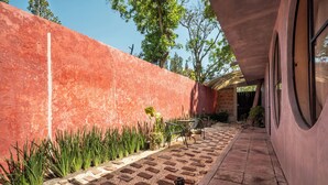 Un camino que lleva a un edificio con una pared roja y una zona cubierta con sillas y mesas.