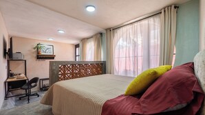 Un dormitorio con cama, escritorio, silla, televisor y ventana con cortinas.