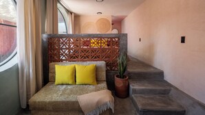 Una escalera conduce a una habitación con un sofá, una planta en maceta y un panel decorativo en la pared.