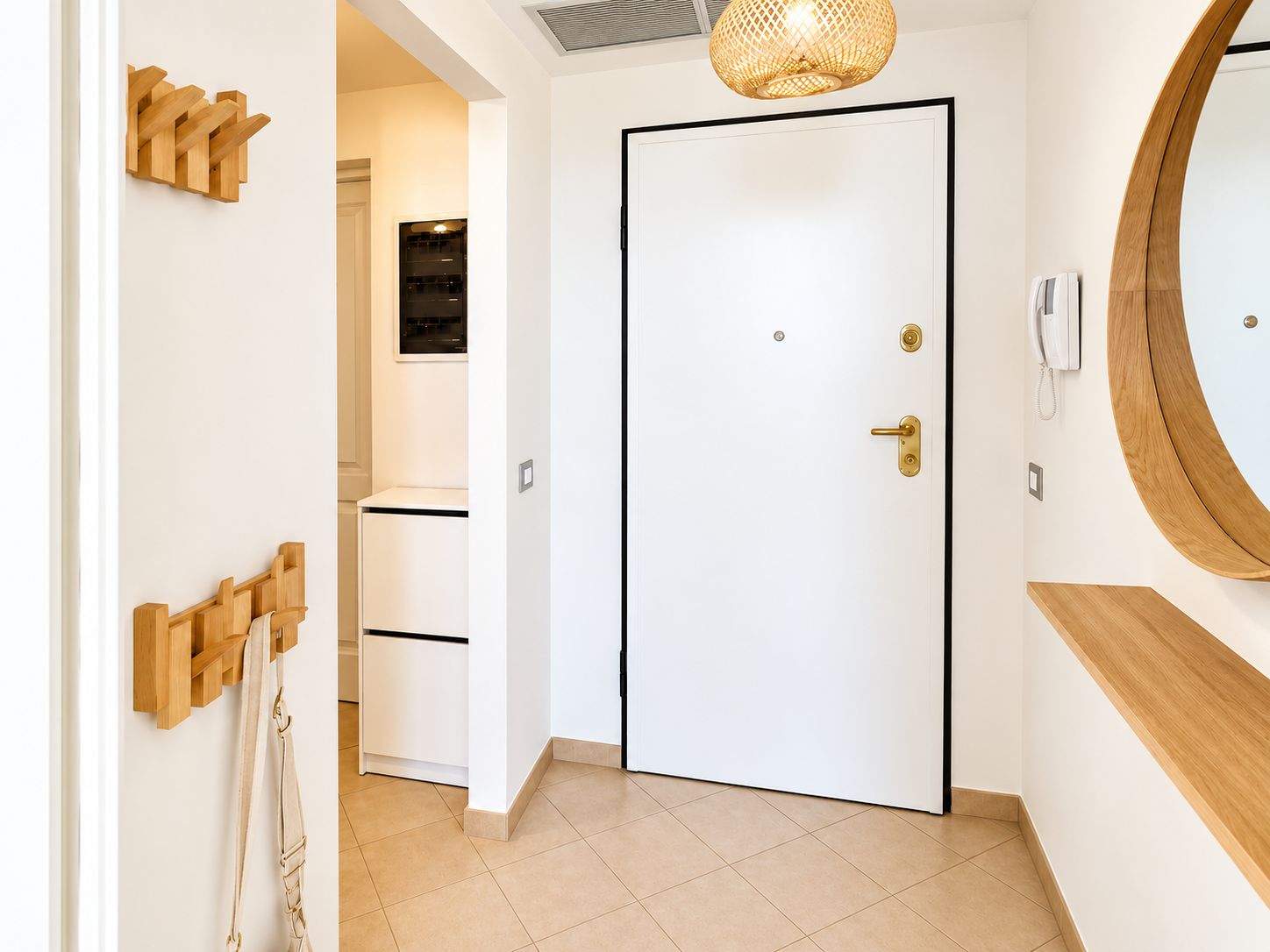 A hallway with a white door, a wooden coat rack, a hanging telephone, and a round mirror on the wall.