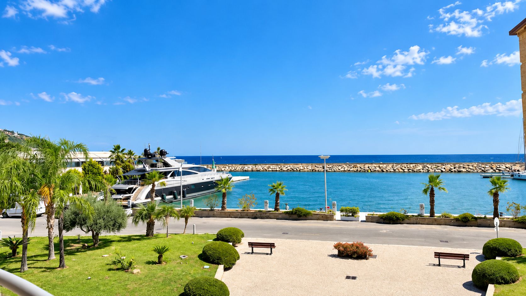 Un puerto deportivo con yates, un rompeolas rocoso y un cielo azul despejado.