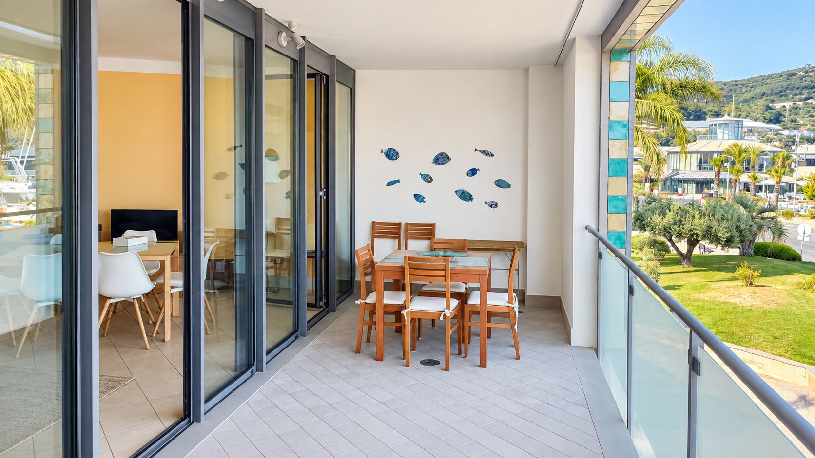 Un balcón con mesa y sillas, una puerta de vidrio que da a una habitación y vistas del entorno.