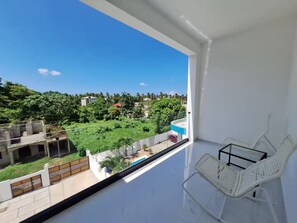 A balcony with a white chair and a view of a green landscape and buildings. - Modern/Lux penthouse In front of rooftop pool (Las Terrenas)