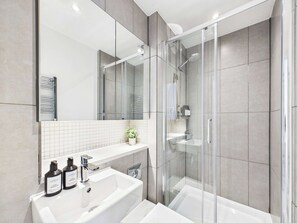 Een moderne badkamer met een douchecabine van glas, een wit wastafelmeubel en een grote spiegel.