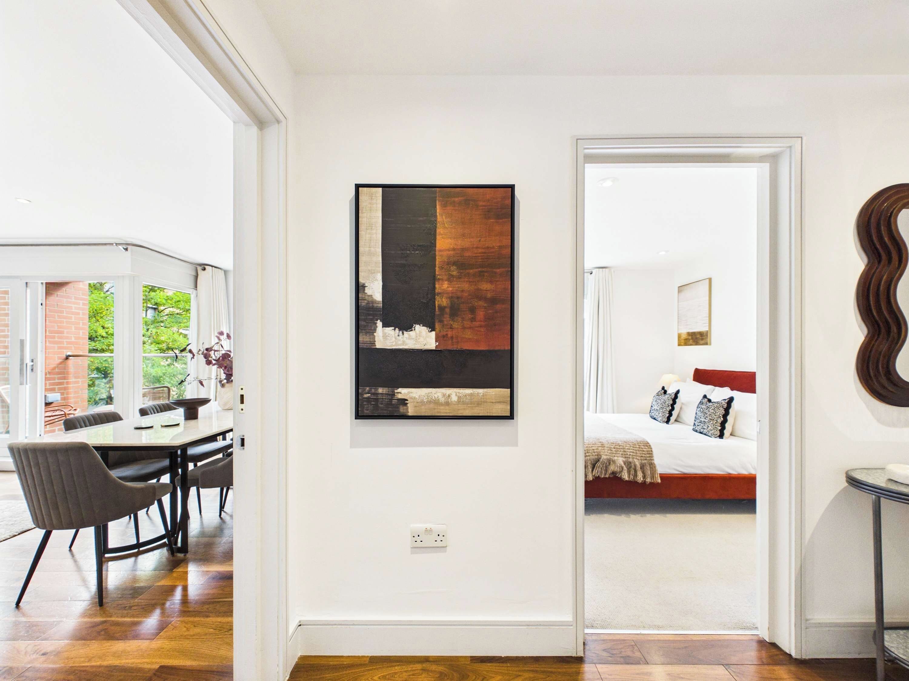 A modern interior with a dining area, a painting, and a bedroom visible through an open door.