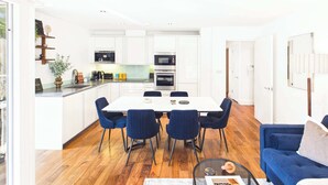 A modern kitchen with white cabinets, a dining table with chairs, and a blue sofa in the living area. - Westminster Spacious 2BR Apartment with Balcony (Greater London)