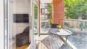 A balcony with a glass door, a small round table with a potted plant, and a chair. - Westminster Spacious 2BR Apartment with Balcony (Greater London)